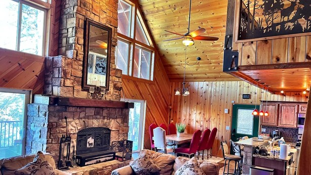 A cozy cabin interior with a stone fireplace, wooden ceiling, and a dining area with red chairs. - Luxury 2 Story Crown King Cabin, Large balcony, Hiking, Fishing, Mountain Views  (Crown King)
