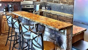 A kitchen with wooden cabinets, a granite countertop, a built-in oven, a microwave, a refrigerator, and three bar stools. - Luxury 2 Story Crown King Cabin, Large balcony, Hiking, Fishing, Mountain Views  (Crown King)