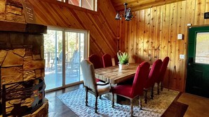 A spacious dining area with a wooden table and red chairs, a stone fireplace, and large windows allowing natural light. - Luxury 2 Story Crown King Cabin, Large balcony, Hiking, Fishing, Mountain Views  (Crown King)