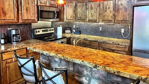 A kitchen with wooden cabinets, a granite countertop, a stove, a microwave, and two pendant lights. - Luxury 2 Story Crown King Cabin, Large balcony, Hiking, Fishing, Mountain Views  (Crown King)