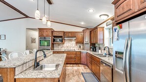 Una cucina moderna con piani in granito, mobili in legno, elettrodomestici in acciaio inossidabile e illuminazione a sospensione.