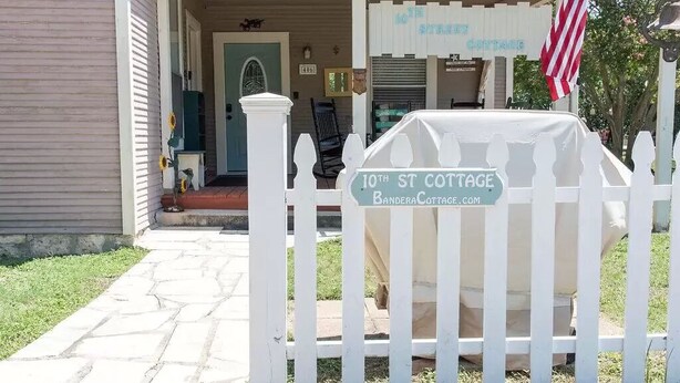 Une clôture blanche en bois avec des piquets, sur laquelle est accrochée une plaque indiquant « 10th St Cottage », et un drapeau américain.