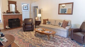 Un salon avec une cheminée, un fauteuil en cuir, un canapé et une table basse.