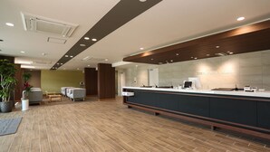 Zona de recepción con piso de madera, un mostrador de recepción y un área de asientos con sillas y una mesa.