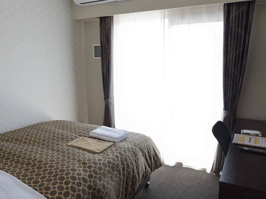 A hotel room with a bed, a desk with a telephone and a coffee maker, and a TV mounted on the wall.