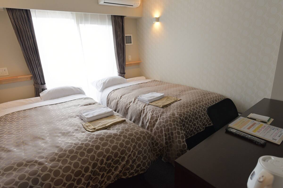 Ett hotellrum med två sängar, ett skrivbord och ett fönster med gardiner.
