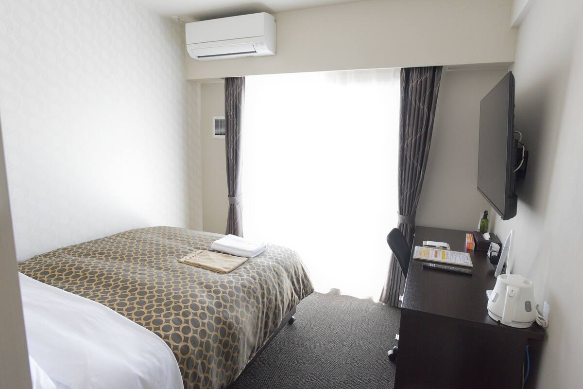 Ett hotellrum med en säng, ett skrivbord med en dator, en TV och en luftkonditioneringsanläggning.