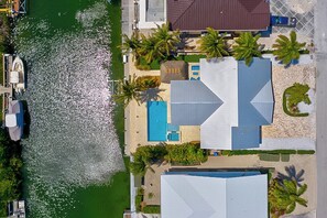 An aerial view of a coastal property with a swimming pool, palm trees, and a boat dock. - P18 - Spectacular 4 bedroom home with dockage and oversized private pool in Key Colony! (Key Colony Beach)