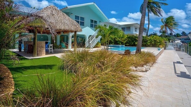 A resort with a pool, a thatched-roof structure, and palm trees. - P18 - Spectacular 4 bedroom home with dockage and oversized private pool in Key Colony! (Key Colony Beach)
