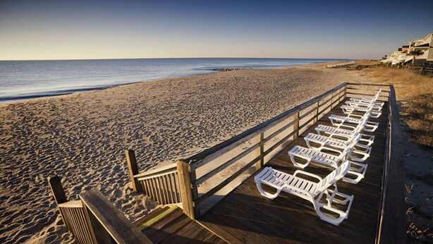 A wooden boardwalk with white lounge chairs along the beach. - Edisto Beach 1BR w/Beach Access (Edisto Island)