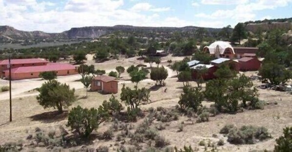 Zona rural con vegetación escasa y algunos edificios, incluyendo una estructura grande de color rojo y construcciones más pequeñas también rojas.