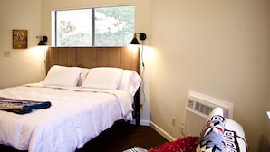 A neatly made bed with white linens, a window with blinds, a wall-mounted lamp, and a radiator. - Authentic Native American Hogan Experience near Chaco Cultural Historical Park (Counselor)