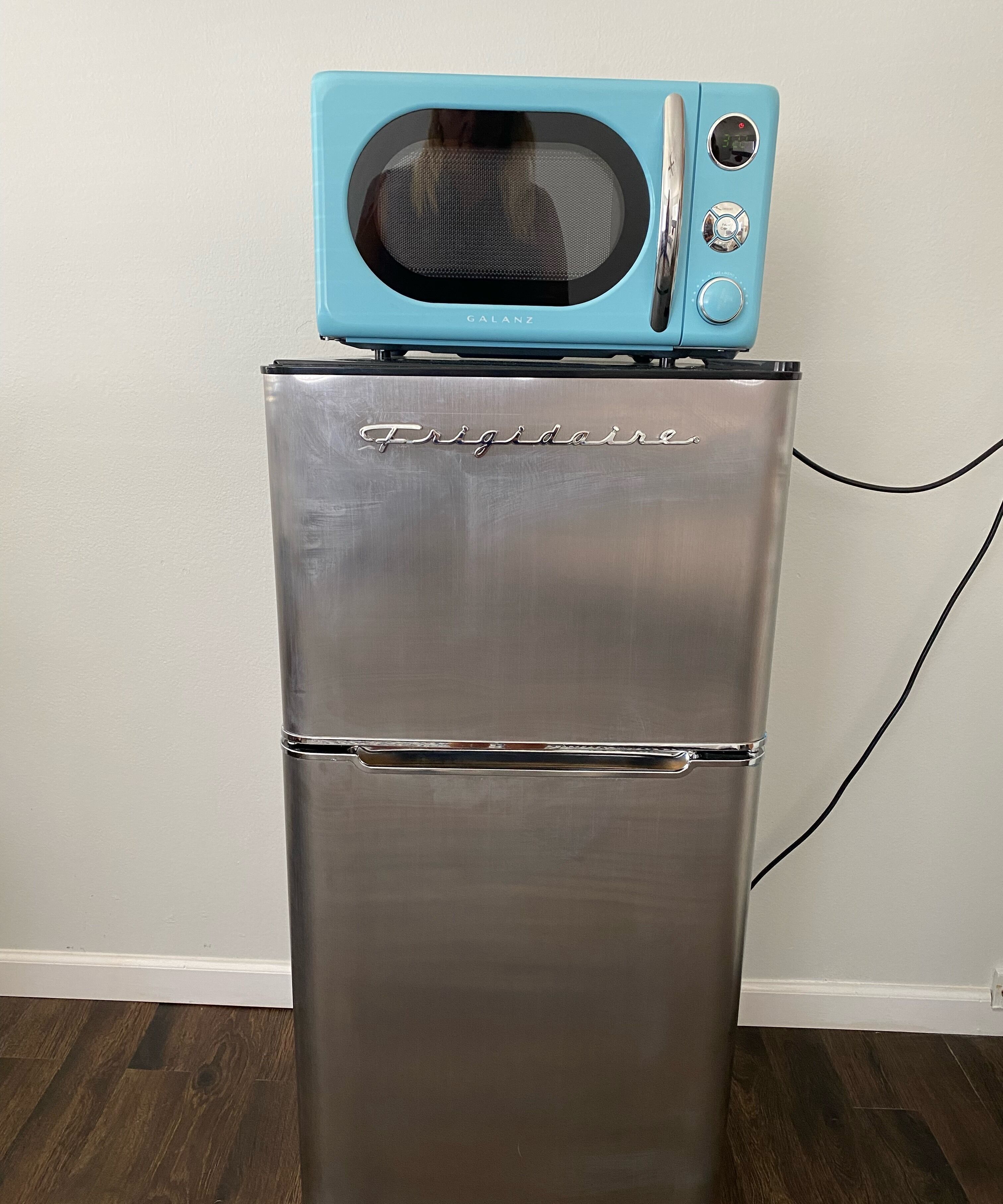 A stainless steel refrigerator with a blue microwave on top.