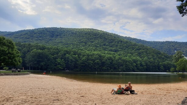 Une plage de sable bordée d’un lac, avec des collines boisées en arrière-plan.