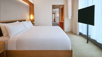 A modern hotel room with a large bed, a flat-screen TV, and a view of the bathroom through an open door.