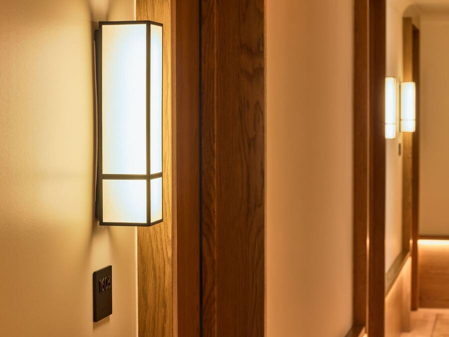 Een gang met een houten deuropening en een wandlamp.