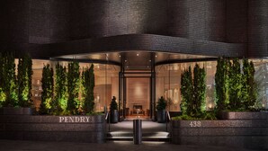 Ingresso moderno di un edificio con facciata curva, area reception con posti a sedere e il nome "PENDRY" esposto sulle scale.