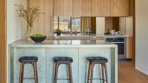 A modern kitchen with wooden cabinets, a large island with stools, and a view of the city through the window.