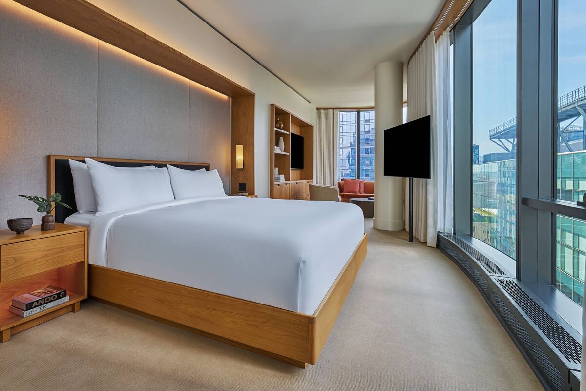 A modern hotel room with a large bed, bedside tables, a TV, and a city view.