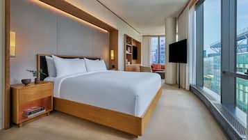 A modern hotel room with a large bed, bedside tables, a TV, and a city view.