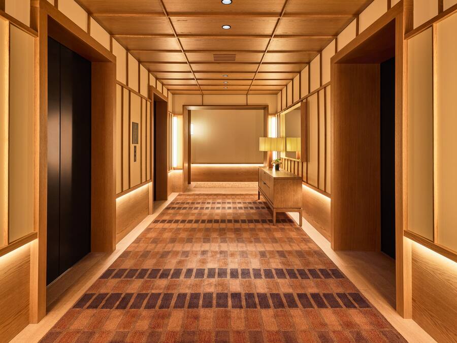 A hallway with wooden paneling, a checkered carpet, and a mirror on the right wall.