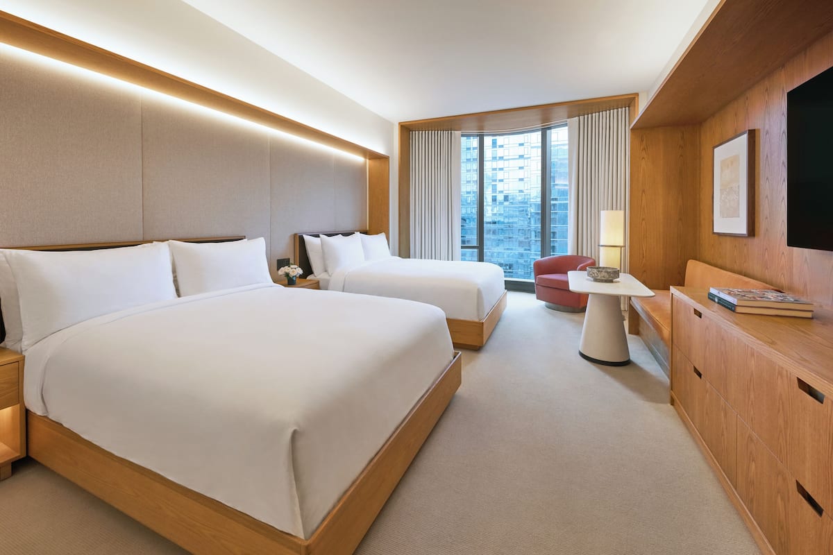 A hotel room with two beds, a desk, a chair, a TV, and a window with curtains.