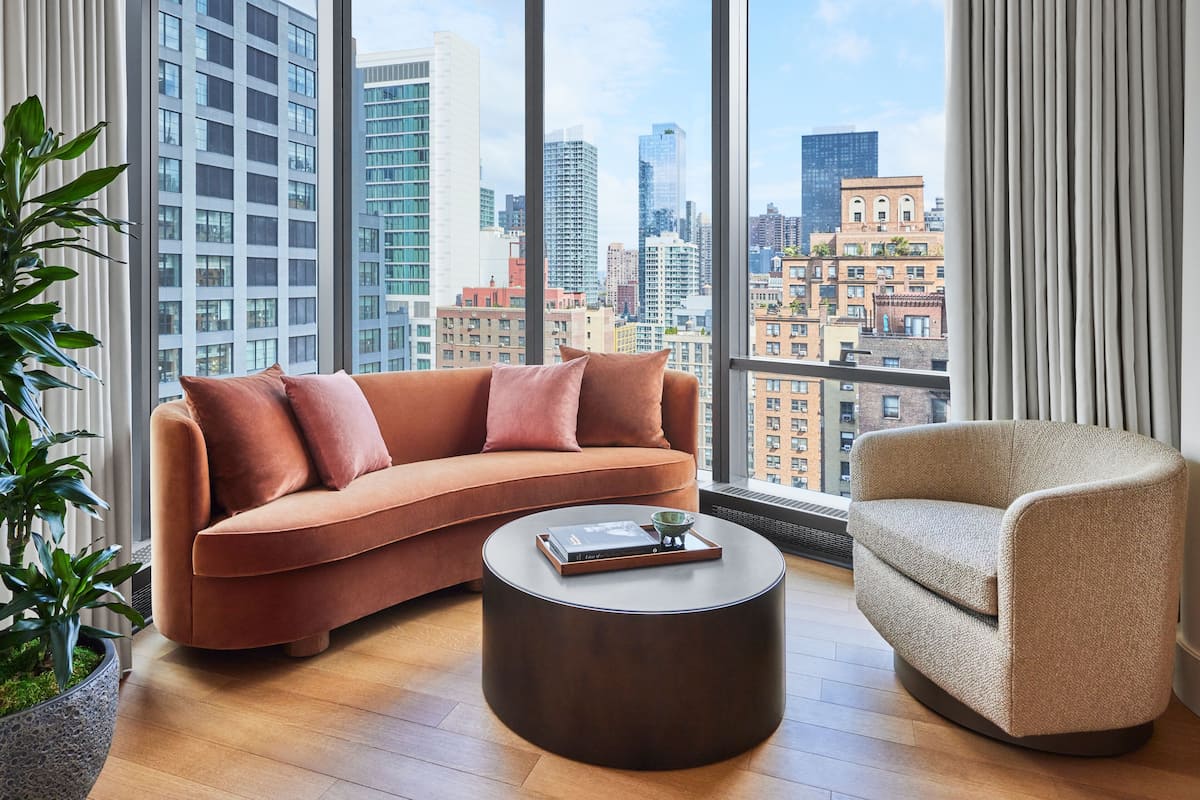 A modern living room with a curved sofa, a round coffee table, and a chair, featuring a city view through large windows.