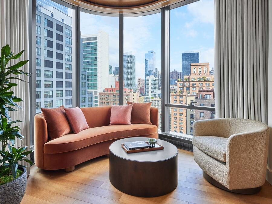 A modern living room with a curved sofa, a round coffee table, and a chair, featuring a city view through large windows.