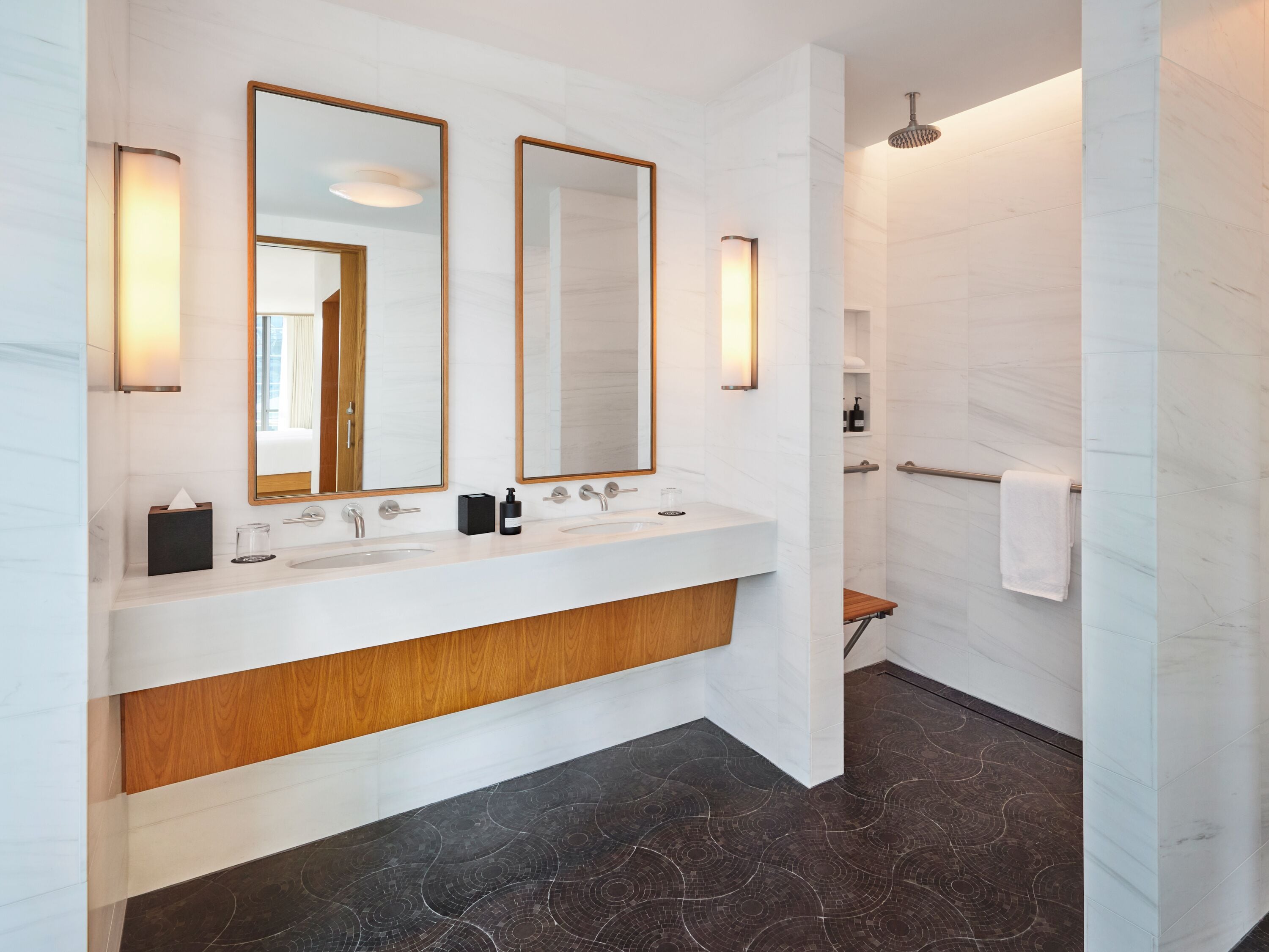 Een moderne badkamer met een wit marmeren wastafelmeubel, twee spiegels, een houten aanrechtblad en een donkere, patroonrijke vloer.