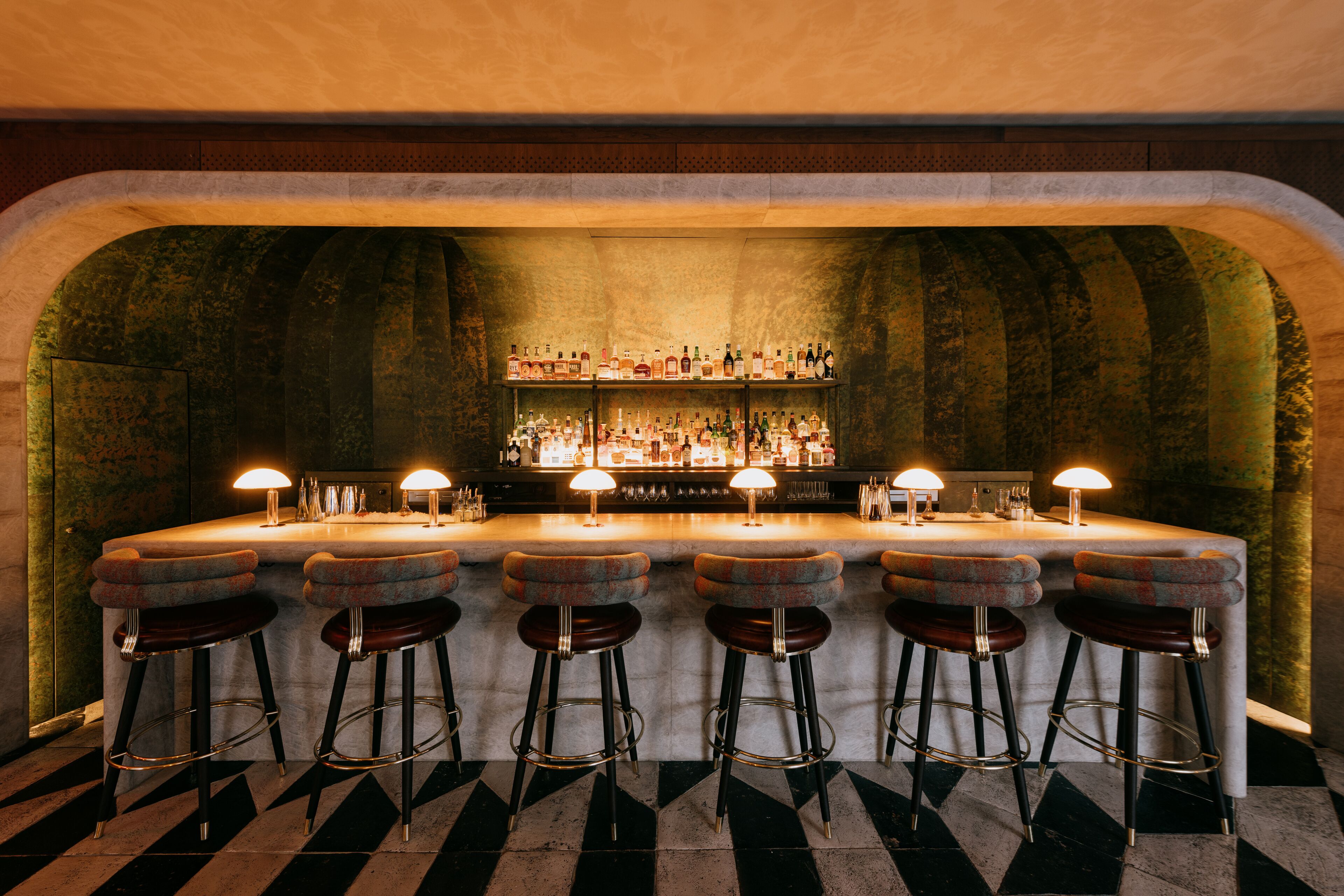 A bar area with a stone archway, bar stools, and a well-stocked shelf of bottles.