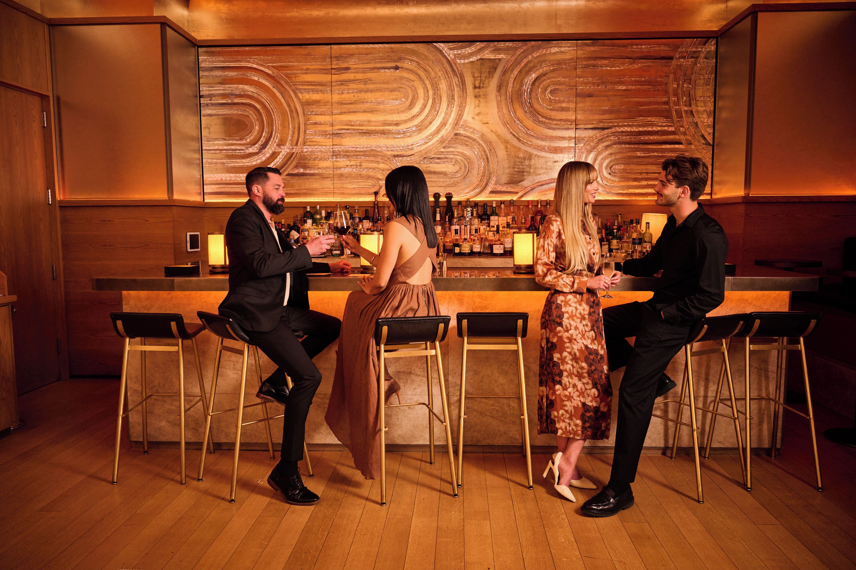 A bar area with wooden flooring, bar stools, and a bar counter with various bottles.