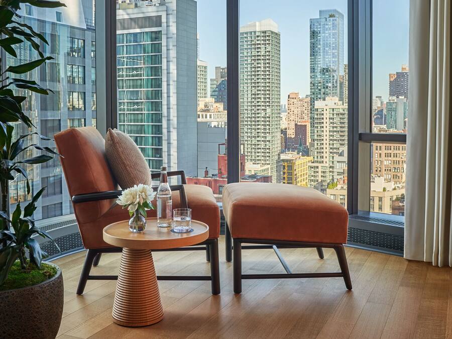 A modern room with a large window, a leather chair, a small table with a vase of flowers, and a bottle of water.