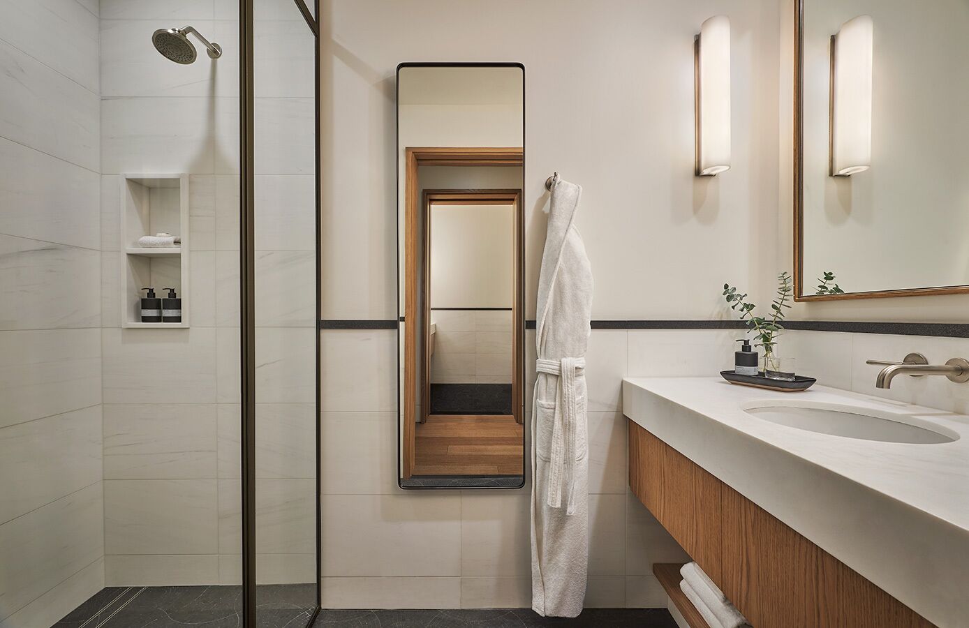 Un bagno moderno con cabina doccia in vetro, uno specchio grande, un mobile vanità in legno e un lavandino bianco.