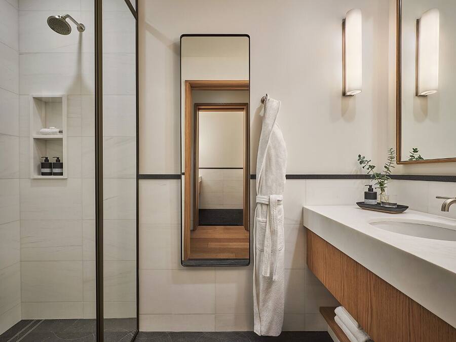 Un bagno moderno con cabina doccia in vetro, uno specchio grande, un mobile vanità in legno e un lavandino bianco.