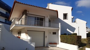 Een modern huis met twee verdiepingen, een witte gevel, een balkon met metalen hekwerk en een garage.