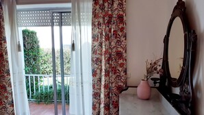 Een kamer met een schuifglazen deur die uitkomt op een balkon, een spiegel en een roze vaas met gedroogde planten.