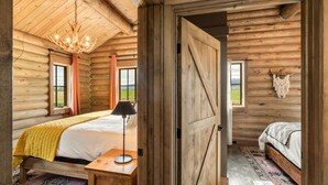 Une chambre dans un chalet en rondins, avec un lit, une lampe et une vue sur l’extérieur.