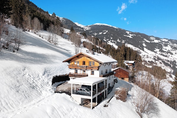 Une maison de style chalet dotée d’un balcon, d’un abri-voiture couvert et offrant une vue sur des montagnes enneigées.