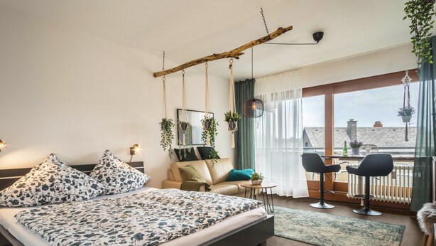 A modern bedroom with a bed, a sofa, a small table, and a balcony with chairs.