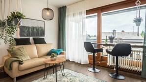 A modern living room with a sofa, two chairs, a coffee table, and a view of the city through large windows.