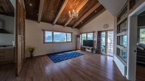 Un'ampia stanza con pavimento in legno, grandi finestre, un lampadario e un televisore a schermo piatto.