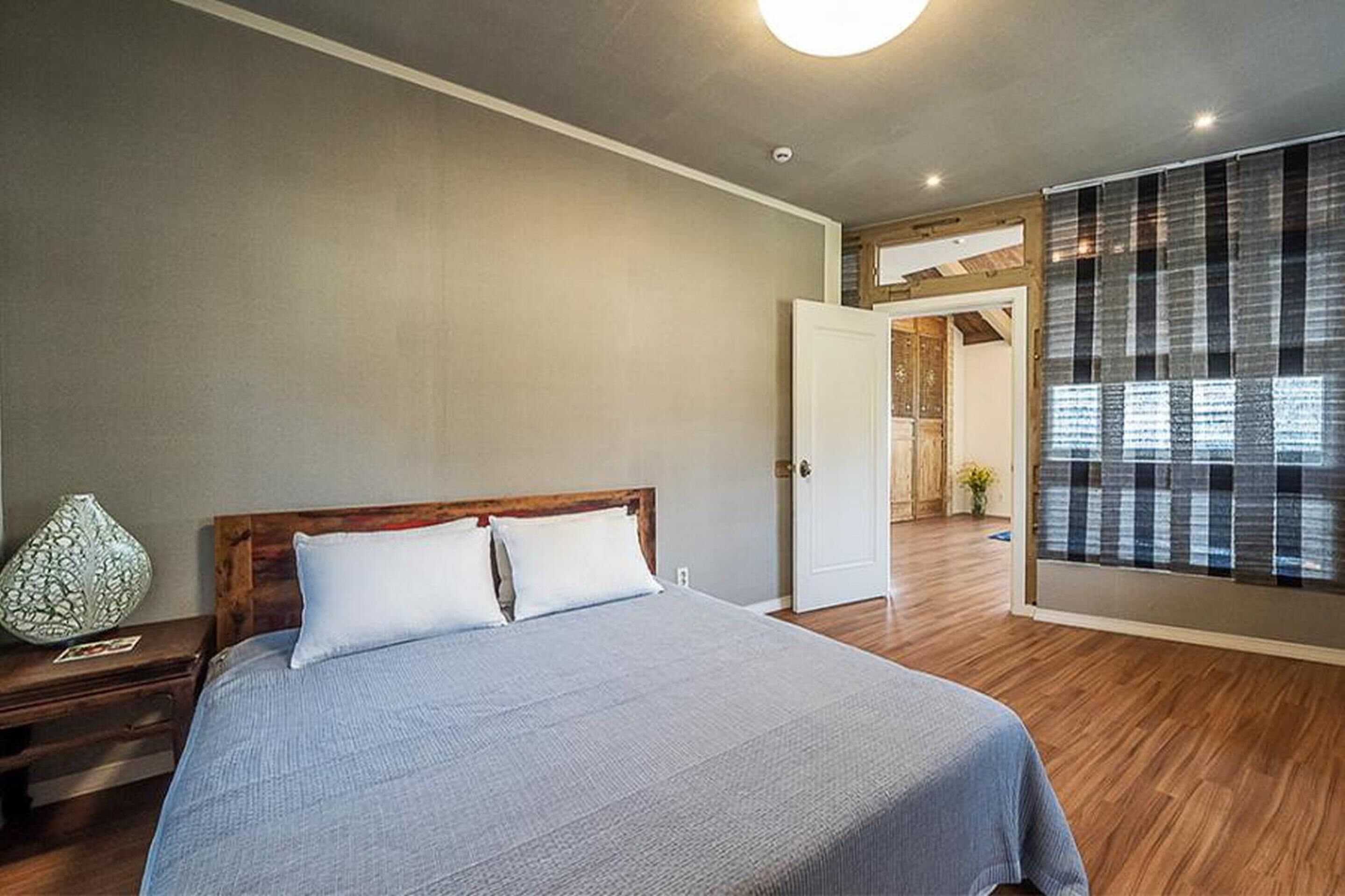 A bedroom with a large bed, wooden headboard, and a nightstand with a lamp.
