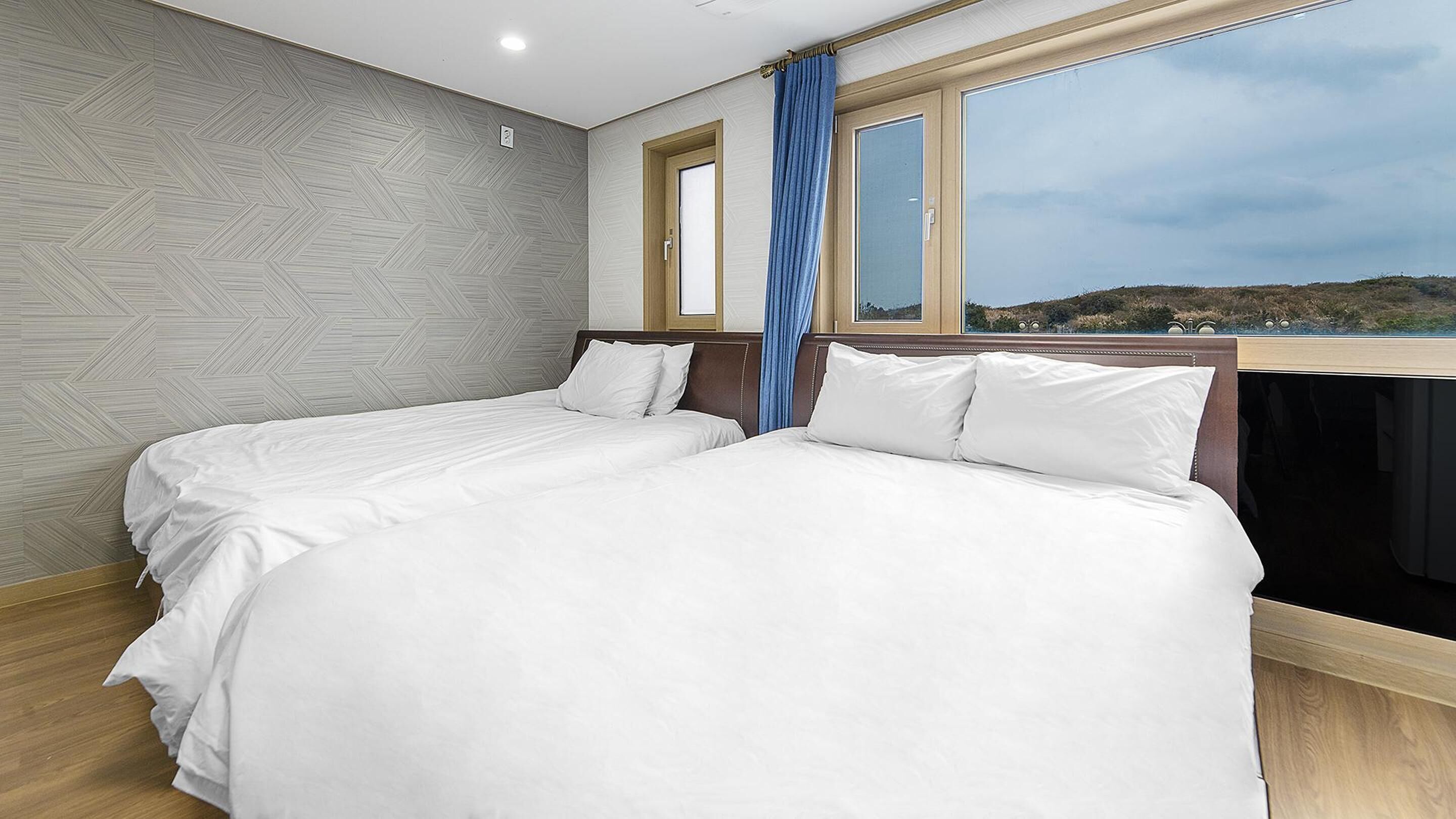 A hotel room with two beds, a large window with a view of the countryside, and a patterned wall.