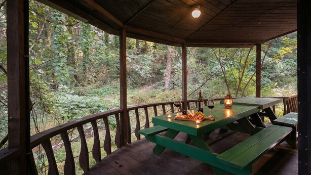 A wooden deck with a green picnic table set up, surrounded by a wooden railing, overlooking a forested area. - Gapyeong Benest Group Pension (Gapyeong)