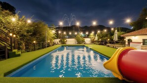 A swimming pool with a slide, surrounded by greenery and string lights. - Gapyeong Benest Group Pension (Gapyeong)