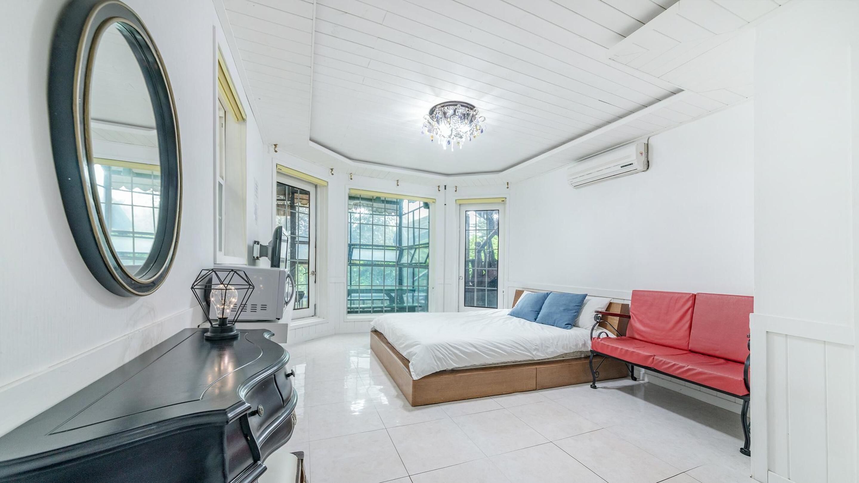 Un dormitorio con cama, sofá rojo, espejo grande y candelabro.