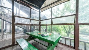 A green wooden table with chess pieces and a bottle, set in a room with large windows overlooking a forested area. - Gapyeong Benest Group Pension (Gapyeong)