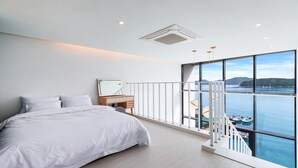 Ein Schlafzimmer mit einem großen Bett, einem Nachttisch, einem Spiegel und Blick auf ein Gewässer durch große Fenster.