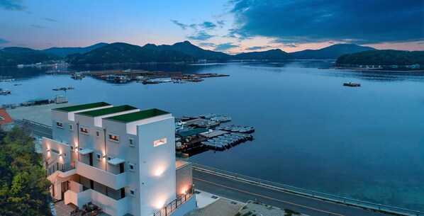 Een modern gebouw met een groen dak, een steiger met boten, en een rustig waterlichaam met bergen op de achtergrond.
