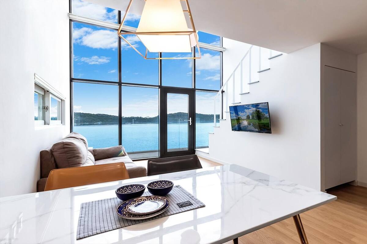 Una cocina moderna con un amplio ventanal con vistas a un lago, una mesa de comedor con cuencos decorativos y un televisor montado en la pared.